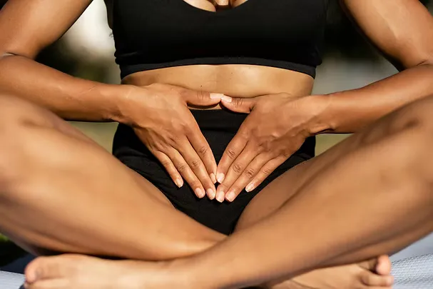 Woman in athletic wear forming a heart shape with her hands over her belly, symbolising gut and body connection