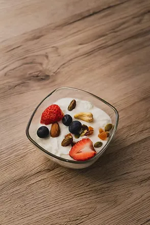 A small bowl of probiotic yoghurt topped with strawberries, blueberries and nuts on a wooden table